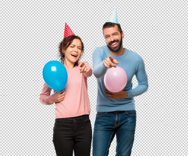 Coppia con palloncini e cappelli di compleanno che puntava il dito contro qualcuno e rideva molto