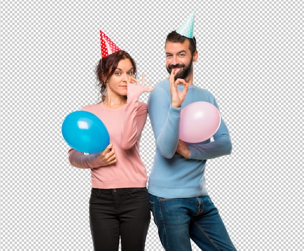 Couple with balloons and birthday hats showing an ok sign with fingers