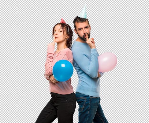 Couple with balloons and birthday hats showing a sign of closing mouth and silence gesture