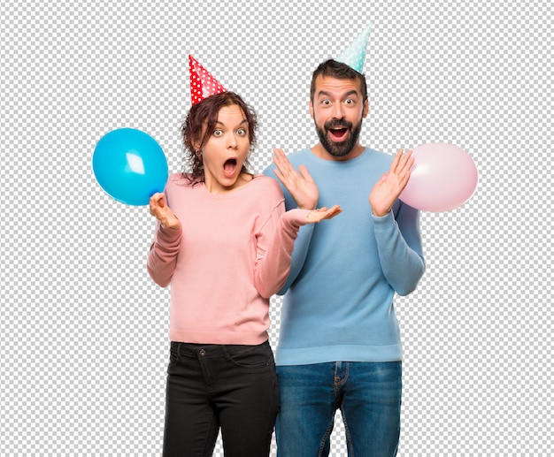 Coppia con palloncini e cappelli di compleanno con espressione sorpresa perché non si aspettano cosa è successo