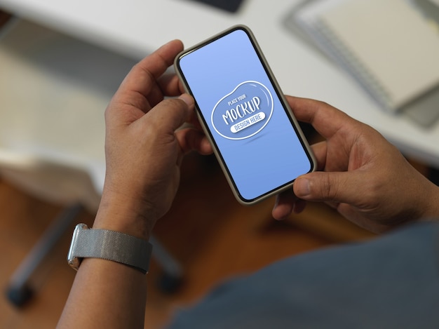 PSD cropped shot of a man using mock up smartphone while standing at worktable in office room