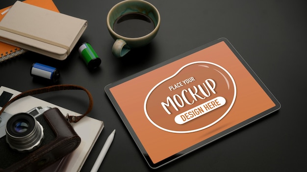 Cropped shot of mock up tablet on black table with camera, stationery, supplies and coffee cup
