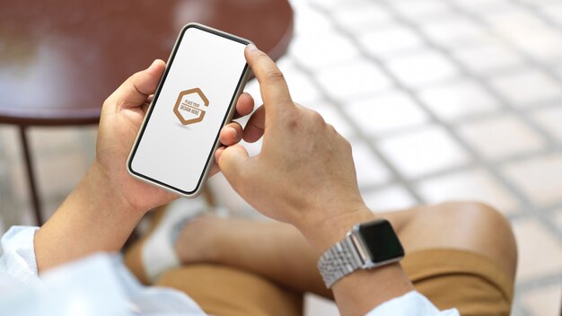 Cropped shot of young man holding mock up smartphone while siting outdoor