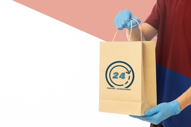 Delivery man hand in medical gloves holding craft paper bag mockup template.