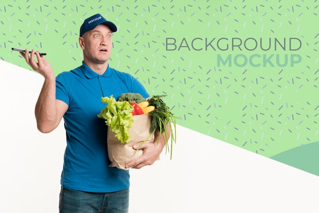 Delivery man holding a box with different vegetables with background mock-up