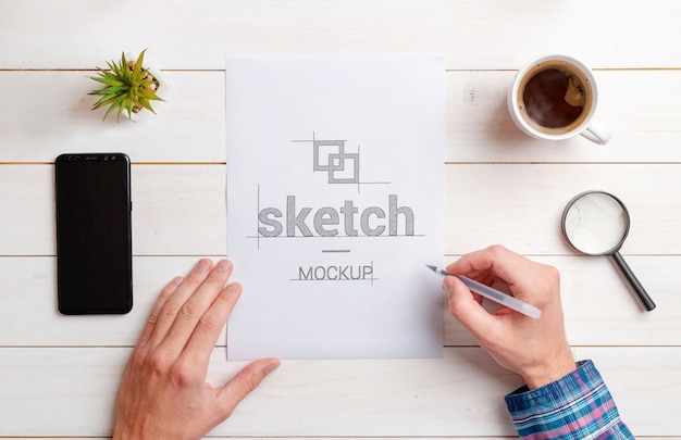 PSD designer sketch mockup. top view, flat lay composition of paper on work desk. phone, coffee mug, plant; magnifier beside. white wooden desk