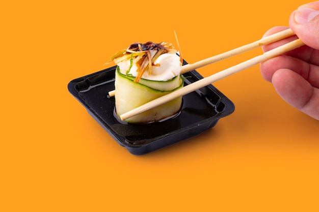 チョップスティックでソヤソースに巻かれたキュウリとクリームチーズを入れた寿司ロールを浸す