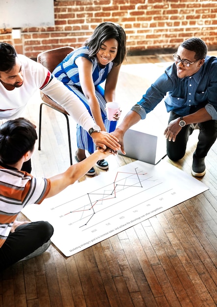 Diverse team stacking hands over a project plan mockup