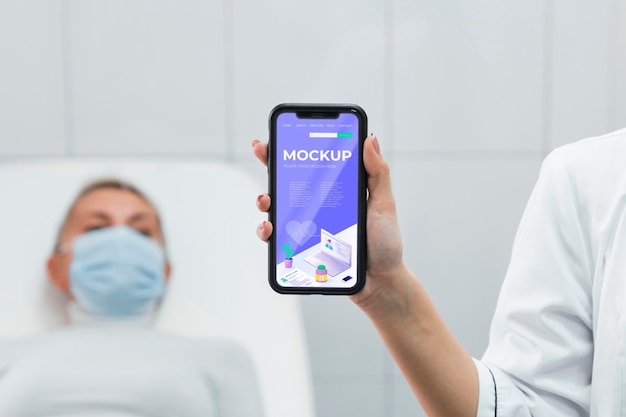 Doctor with face mask holding phone mock-up near patient