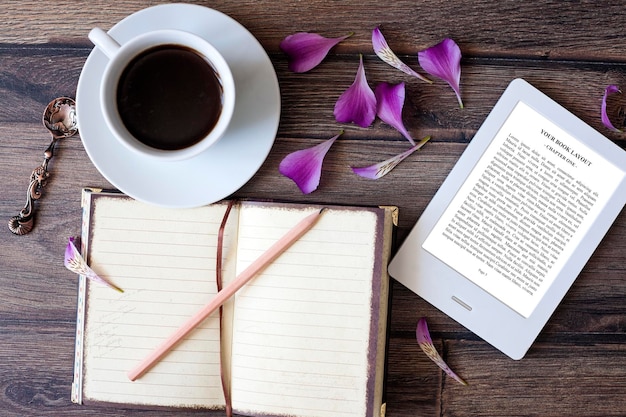 Mockup del lettore di e-book con tazza di caffè, fiori, taccuino e matita su sfondo di legno marrone