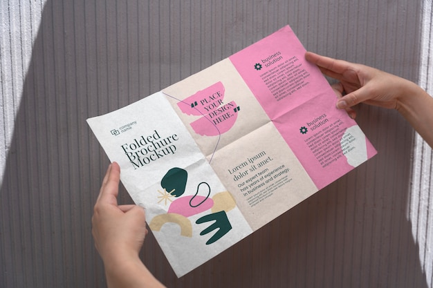 PSD female hands holding trifold brochure mock-up with abstract shapes