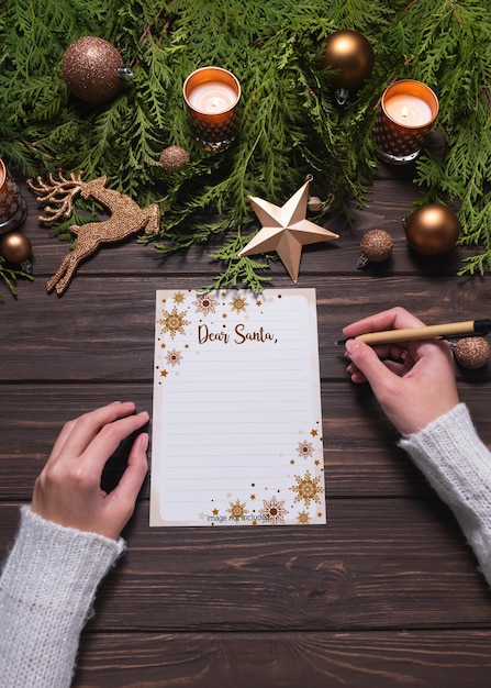 Female hands write christmas postcard or wishlist on wooden background mockup