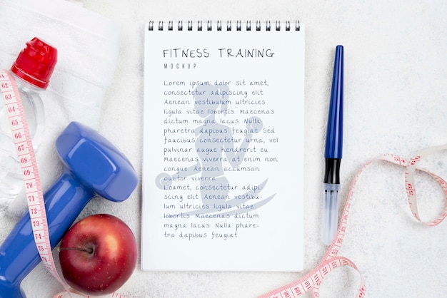 Flat lay of fitness notebook with measuring tape and weight