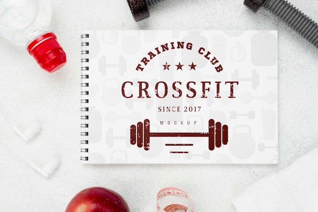 Flat lay of fitness notebook with weights and apple