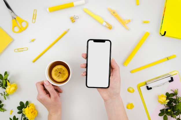 Flat lay hands holding smartphone mock-up with stationery