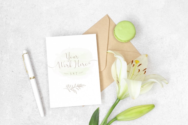 Flat lay invitation card with craft envelope, lily and macarons