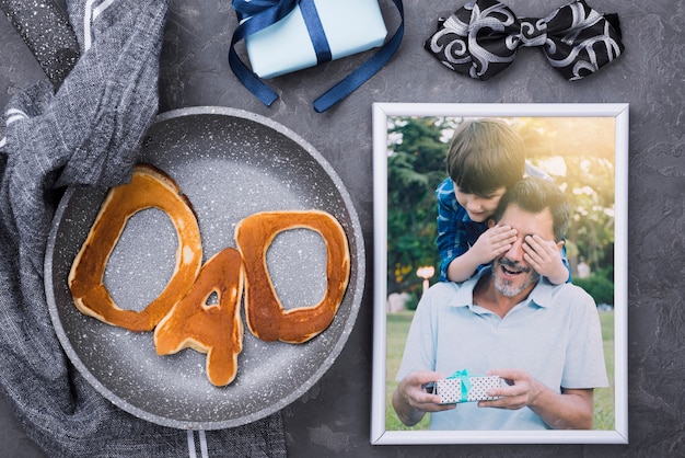 Flat lay of photo with pancakes in pan and gift for fathers day