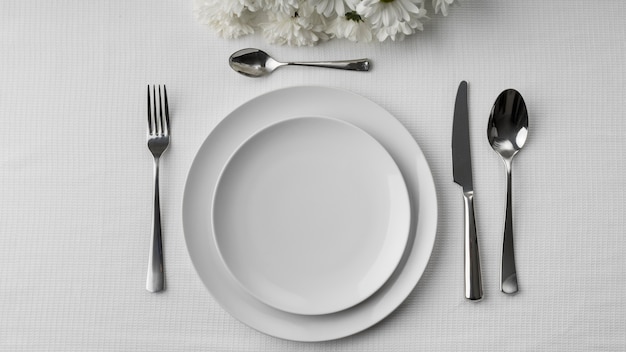 Flat lay of plates on table with cutlery and flowers