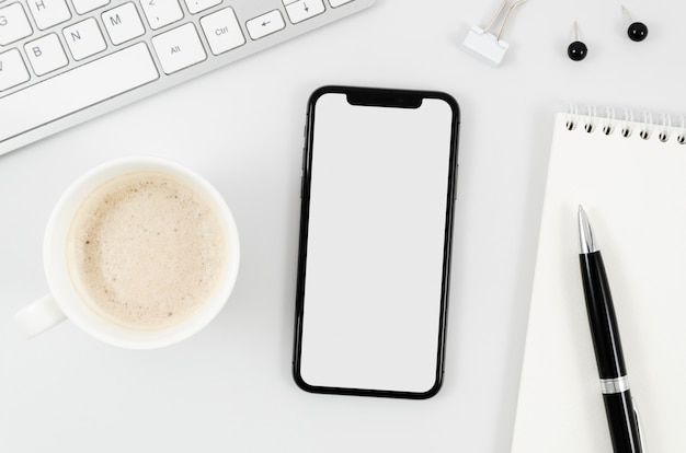 Flat lay smartphone mock-up with empty cup on desk