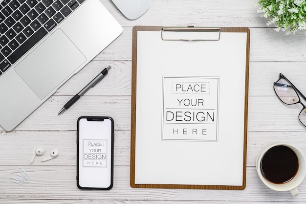 PSD フラットレイ上面図空白のモックアップスマートフォンとラボトップマウスイヤホンペンノートブックと植物を備えたオフィスデスクのクリップボード上の紙あなたのデザインを挿入するための空のスペース