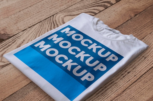 Folded White T-Shirt Over Wood Surface Mockup