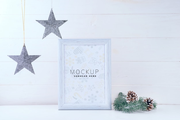 Foto mock up met wit frame, sterren en pijnboomtakken op witte houten achtergrond