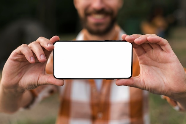 Front view of defocused smiley man holding smartphone while camping