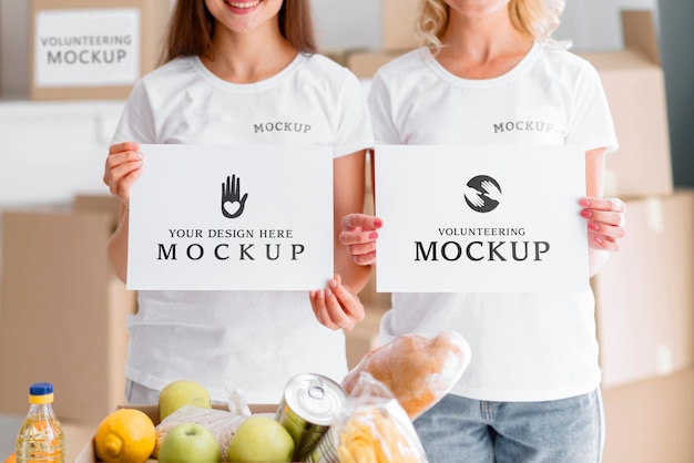 Front view of female volunteers holding blank papers next to food box