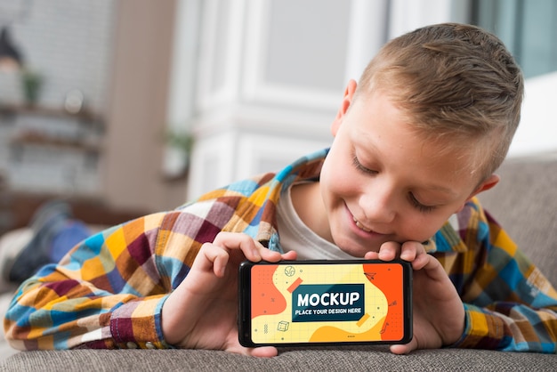 Front view of smiley kid on couch holding smartphone