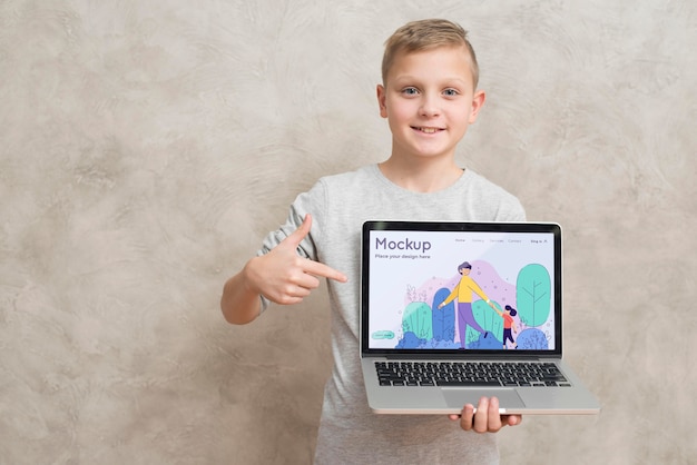 PSD front view of smiley kid holding and pointing at laptop