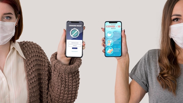 Front view of two women with masks holding smartphones