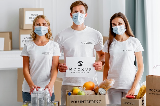 Front view of volunteers with medical masks holding blank paper next to food box