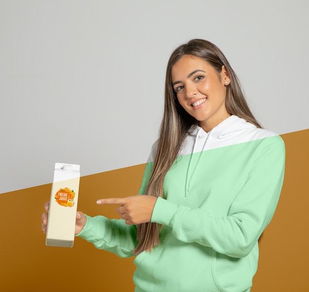 Front view of woman in hoodie pointing at juice carton