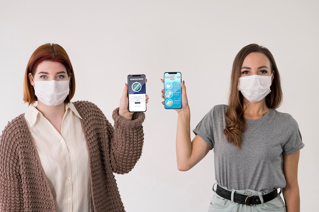 Front view of women with masks holding smartphones