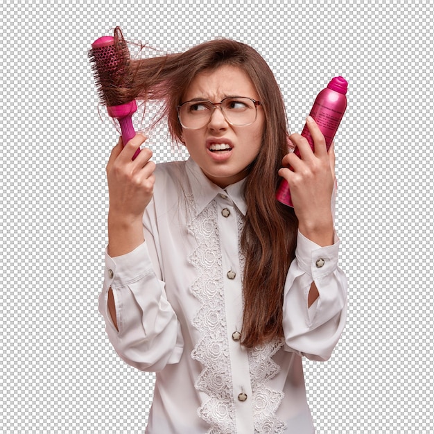 Frustreerde ontevreden vrouw probeert haarborstel uit haar haar te blazen houdt haarspray heeft probleem met haar gekleed in wit hemd fronst met ongenoegen gezicht geïsoleerd op roze muur schoonheid concept