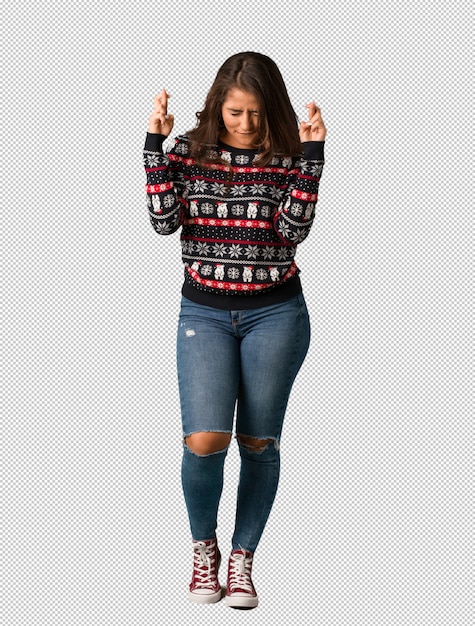 Full body young woman wearing a christmas jersey crossing fingers for having luck