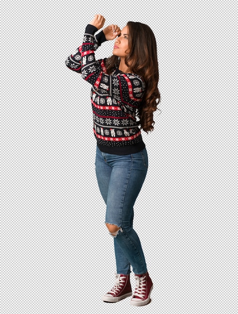 Full body giovane donna che indossa una maglia di natale facendo il gesto di un cannocchiale