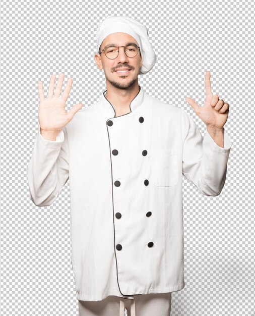 Gelukkige jonge chef-kok die een nummer zeven gebaar met zijn handen doet