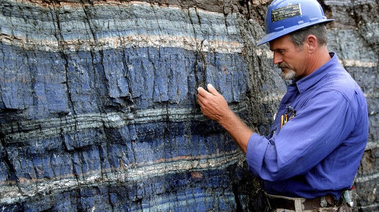 PSD geologist examining layered blue rock formation