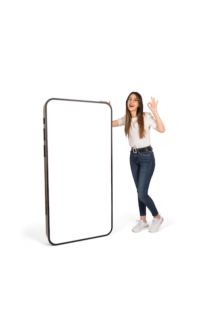 Girl leaning on big smartphone with empty white screen showing ok sign gesture recommending