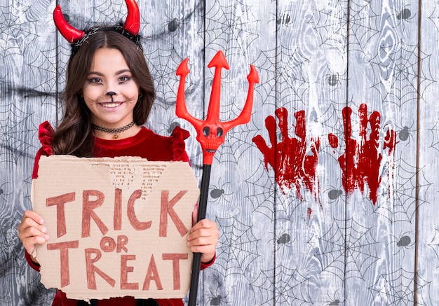 Ragazza con il segno di scherzetto o dolcetto che tiene il tridente del diavolo