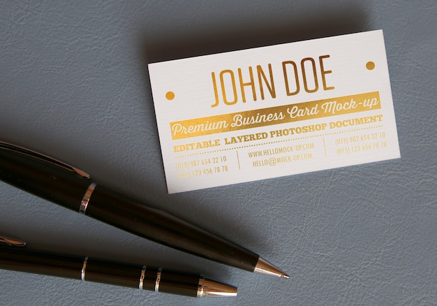 PSD gold pressed letters business card mockup template on leather surface with two premium pens