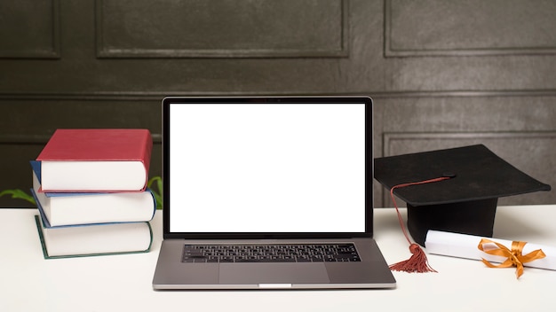 PSD graduation cap and books with laptop mockup