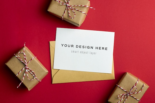 Mockup di biglietto di auguri con scatole regalo di natale su sfondo di carta rossa