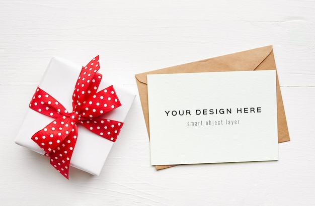 PSD greeting card mockup with envelope and gift box with red ribbon on white table