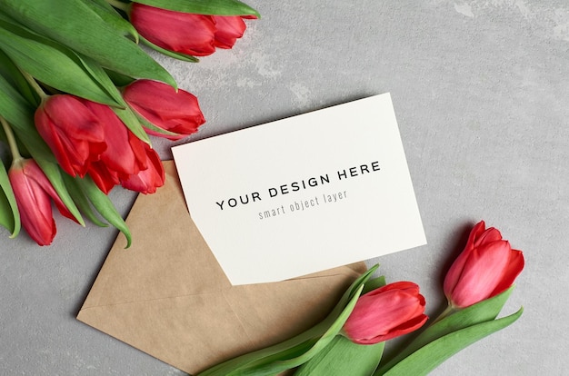 Mockup di biglietto di auguri con busta e bouquet di fiori di tulipano rosso su sfondo grigio