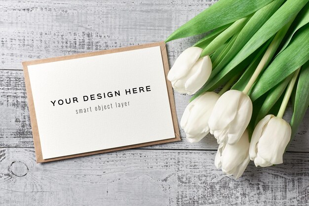 PSD mockup di biglietto di auguri con busta e fiori di tulipano su fondo di legno