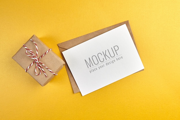 Mockup di biglietto di auguri con confezione regalo su sfondo di carta oro