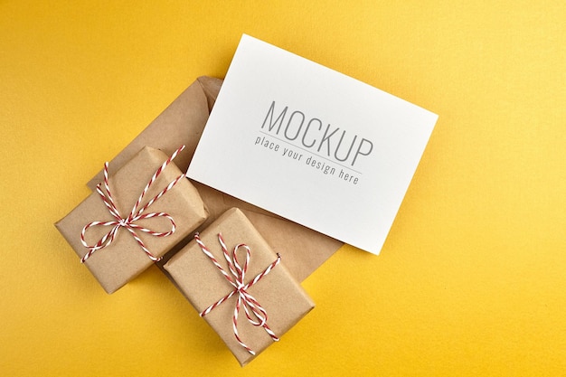 Mockup di biglietto di auguri con scatole regalo su sfondo di carta oro