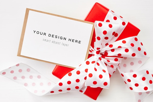 Mockup di biglietto di auguri con confezione regalo rossa con fiocco